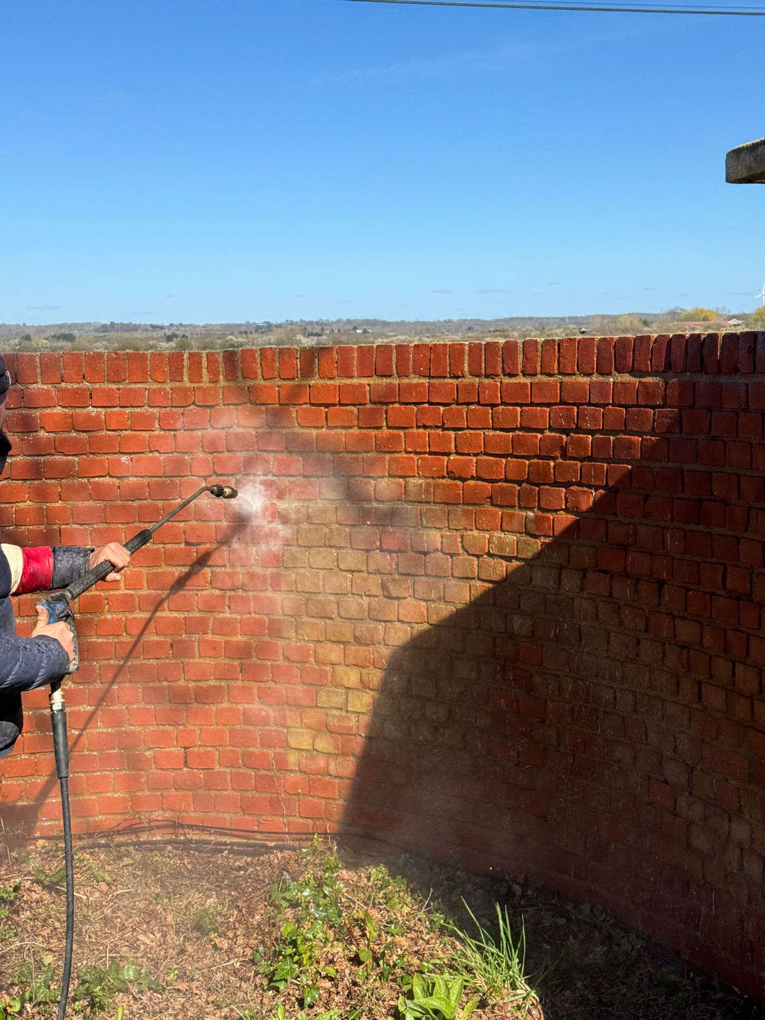 Operator pressure washing a curved brick wall